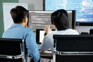 Home 4 Two developers working together in an office, discussing code on a screen. Technology teamwork setting.