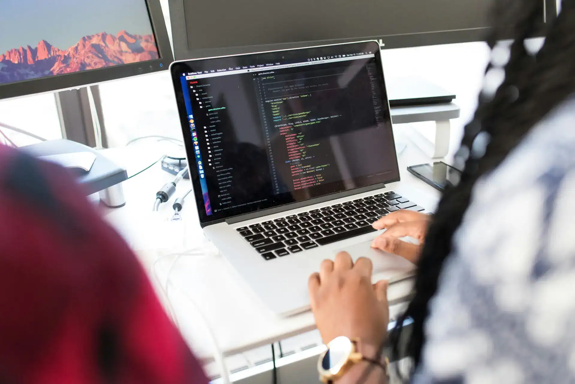 pexels-photo-1181467-1181467 A woman coding on a laptop in a modern office environment with multiple monitors.
